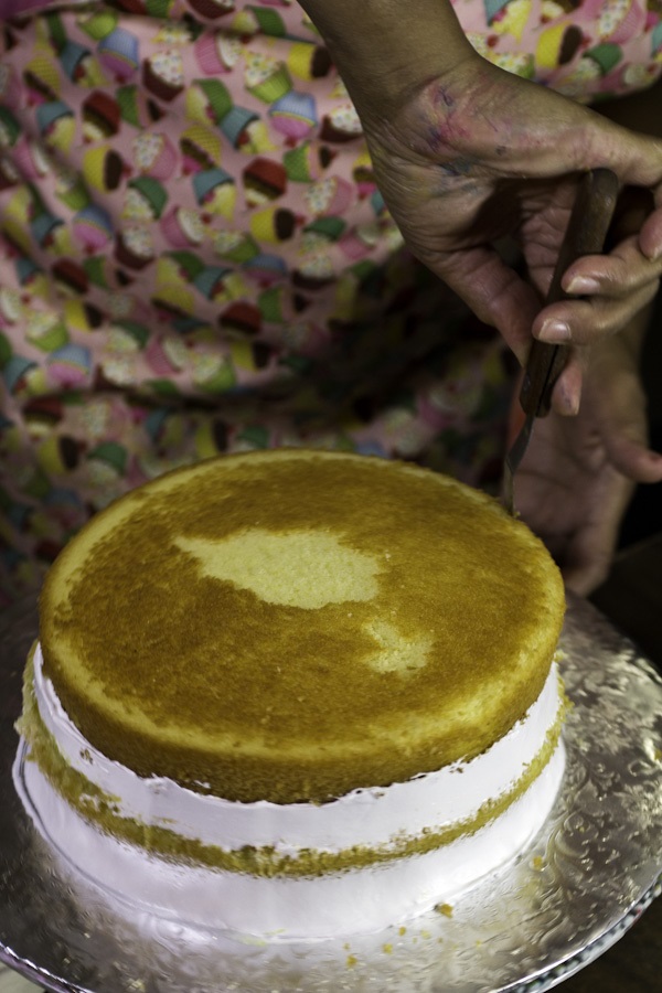 Andujar assembles the cake, putting a cake layer on a cardboard base, spreading on pineapple filling, then adding another layer and suspiro. The suspiro also helps to keep the cake moist, another signature of a good Dominican cake.